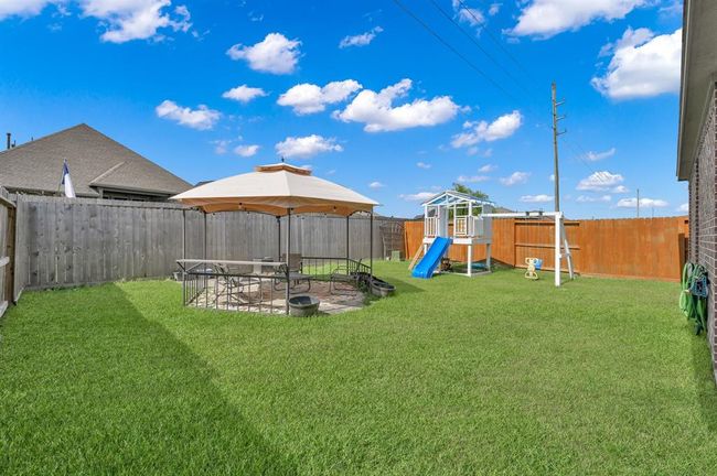 This backyard features a covered patio area with seating, a well-maintained lawn, a swing set, and a brick exterior. It is fully fenced, providing privacy and a safe space for outdoor activities. | Image 30
