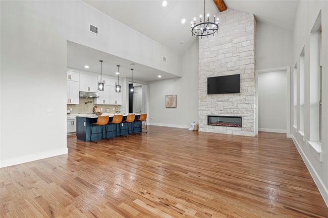 Unfurnished living room featuring high vaulted ceiling, light wood finished floors, a chandelier, beam ceiling, and a fireplace | Image 7