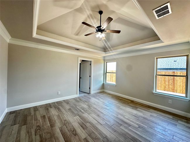 Empty room featuring a tray ceiling, a ceiling fan, dark wood-style flooring, baseboards, and ornamental molding | Image 13