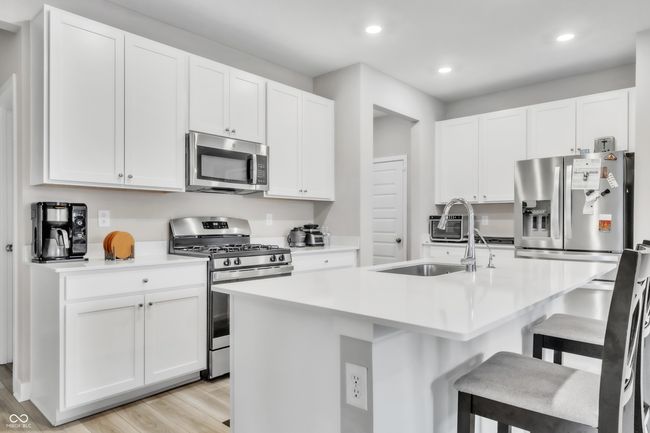 kitchen featuring white cabinets, light countertops, appliances with stainless steel finishes, a kitchen bar, and light wood finished floors | Image 7