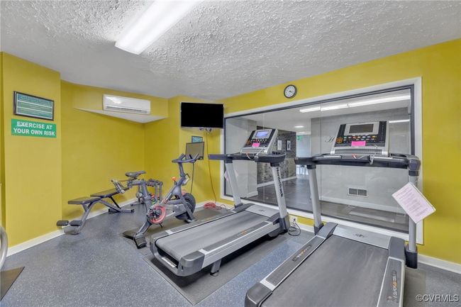 Exercise area featuring a textured ceiling, visible vents, an AC wall unit, and baseboards | Image 26