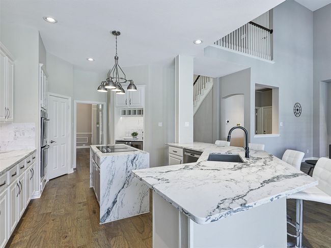 Kitchen featuring a large island, dark wood finished floors, white cabinets, tasteful backsplash, and recessed lighting | Image 17
