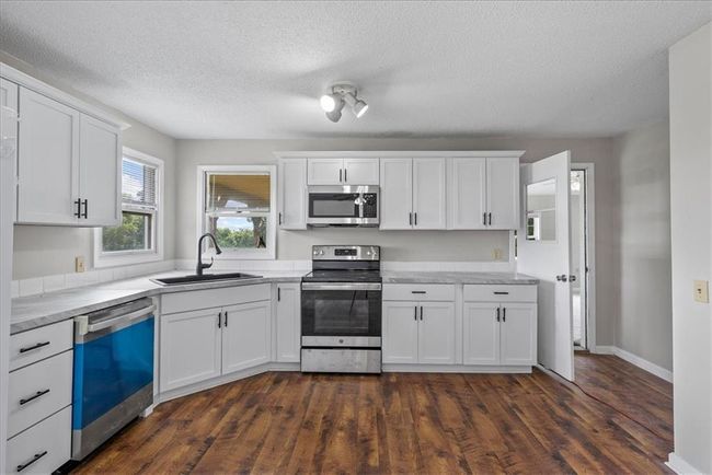 Kitchen with white cabinetry, light countertops, a sink, and stainless steel appliances | Image 59