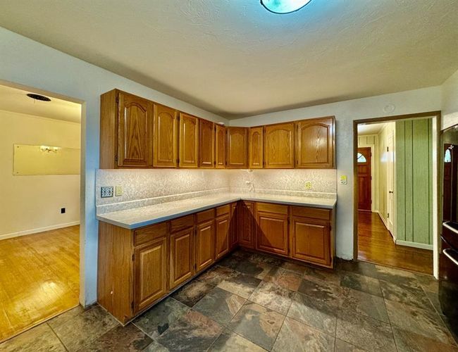 Kitchen featuring brown cabinetry, light countertops, dark stone finish flooring, and tasteful backsplash | Image 10