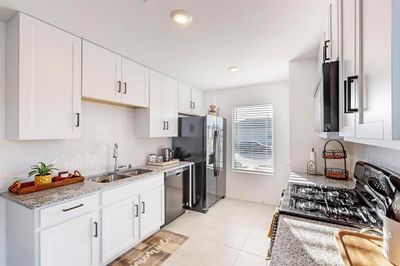 Kitchen featuring light stone countertops, stainless steel appliances, sink, white cabinetry, and light tile patterned floors | Image 3