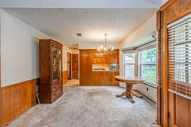 Carpeted dining space with a notable chandelier, a textured ceiling, visible vents, and wood walls | Image 22