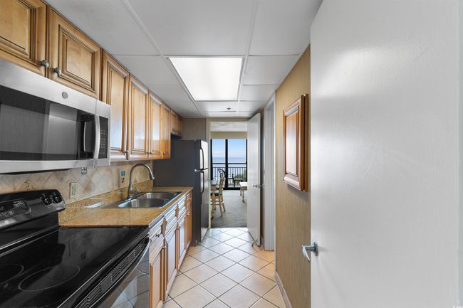 Kitchen featuring black electric range oven, stainless steel microwave, a sink, light tile patterned floors, and baseboards | Image 15
