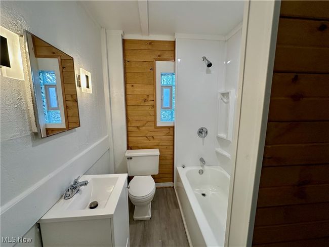 Bathroom featuring toilet, wood finished floors, shower / bathing tub combination, vanity, and wood walls | Image 8