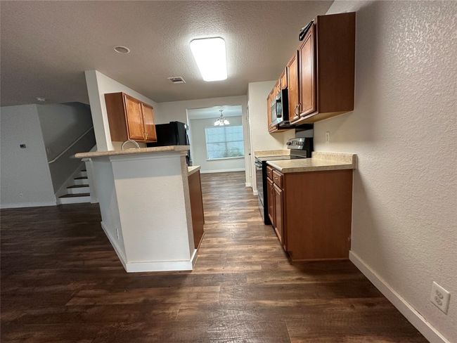 Kitchen with black electric range oven, brown cabinetry, a textured wall, dark wood finished floors, and a textured ceiling | Image 7