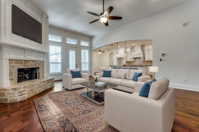 Living room featuring dark wood-type flooring, a stone fireplace, a ceiling fan, and baseboards | Image 4