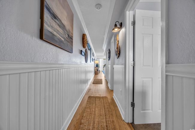 Hall featuring a textured wall, wainscoting, wood finished floors, crown molding, and a decorative wall | Image 4