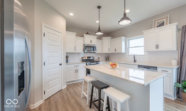 Kitchen featuring stainless steel appliances, a center island, a sink, white cabinetry, and decorative backsplash | Image 8