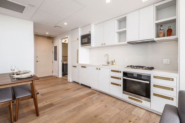 Kitchen featuring stainless steel gas stovetop, oven, open shelves, visible vents, and black microwave | Image 7