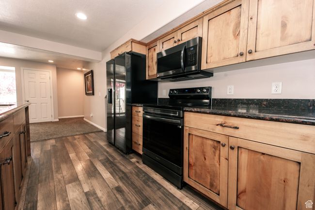 The kitchen features granite countertops, black appliances, an island, LVP floors, and recessed lighting. | Image 23