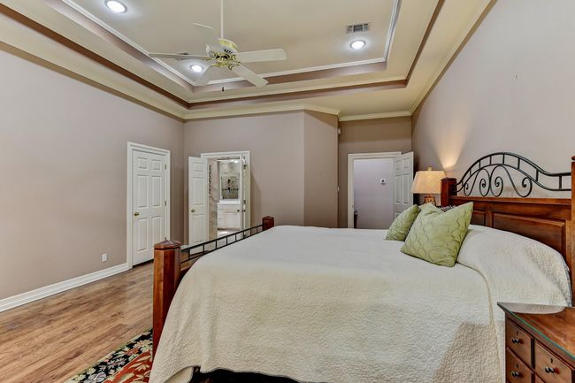 Bedroom with a raised ceiling, visible vents, light wood-style floors, crown molding, and baseboards | Image 16