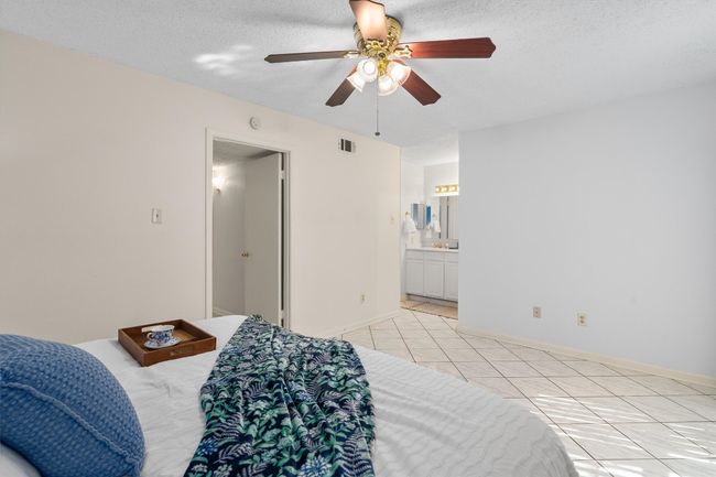 Bedroom featuring baseboards, ensuite bathroom, light tile patterned flooring, visible vents, and ceiling fan | Image 20