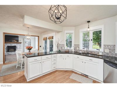 Kitchen with decorative light fixtures, light hardwood / wood-style flooring, dishwasher, and a stone fireplace | Image 3