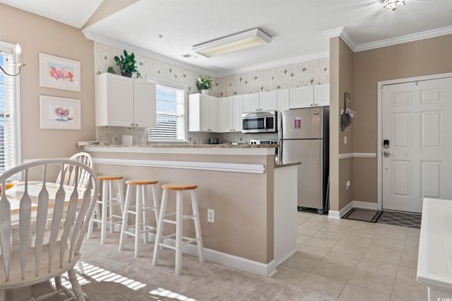 Kitchen with stainless steel appliances, a peninsula, white cabinets, a breakfast bar area, and crown molding | Image 12