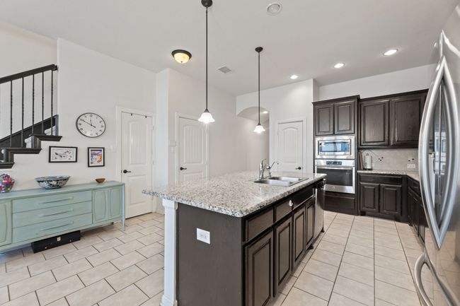 Kitchen featuring stainless steel appliances, a sink, backsplash, light tile patterned flooring, and an island with sink | Image 11