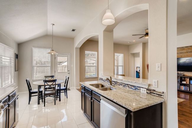 Kitchen with stainless steel dishwasher, ceiling fan, arched walkways, light stone counters, and hanging light fixtures | Image 10