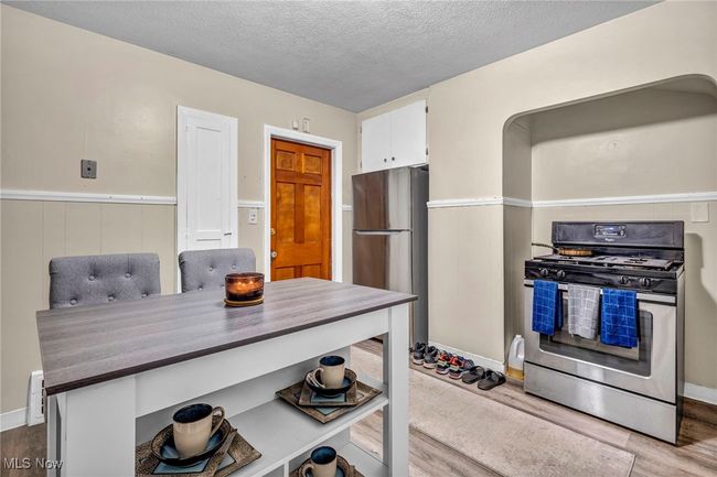 Kitchen with white cabinets, appliances with stainless steel finishes, wood finished floors, and a textured ceiling | Image 5