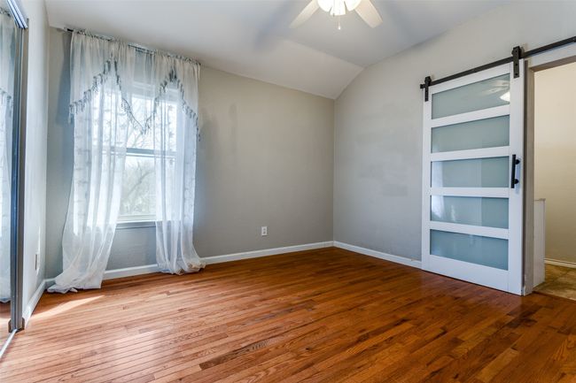 Unfurnished bedroom featuring vaulted ceiling, baseboards, a barn door, and wood-type flooring | Image 21