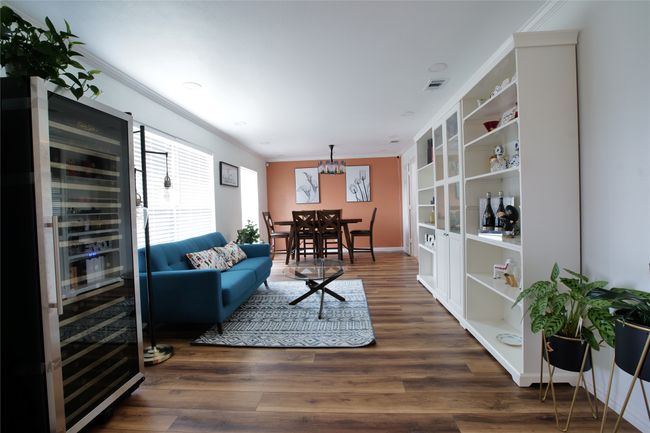 Living room with wine cooler, ornamental molding, wood finished floors, a chandelier, and built in shelves | Image 6