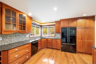 Kitchen with light hardwood / wood-style flooring, decorative backsplash, black appliances, crown molding, and dark stone countertops | Image 2