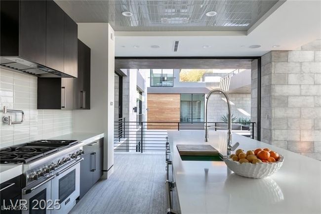 Kitchen featuring double oven range, wall chimney range hood, light wood-style flooring, dark cabinets, and light countertops | Image 21