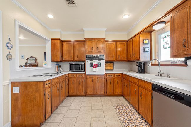 Kitchen with stainless steel appliances, brown cabinetry, light countertops, and ornamental molding | Image 10