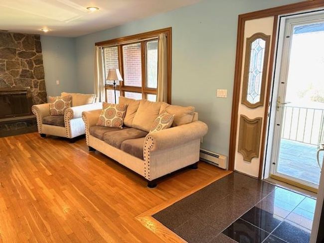 Living room with hardwood / wood-style flooring, a baseboard radiator, and a stone fireplace | Image 7