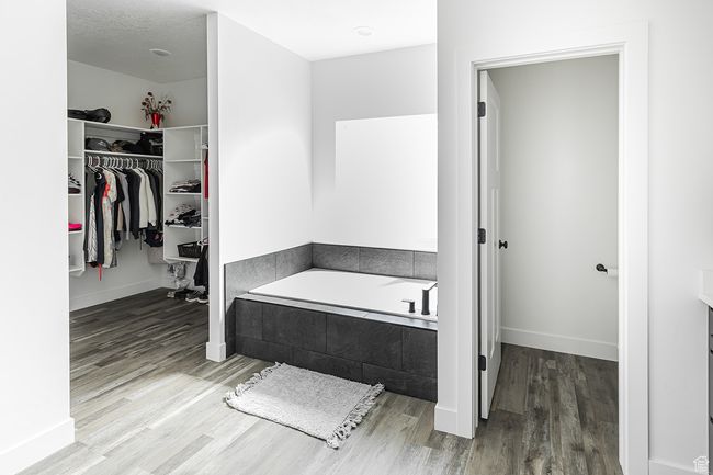Bathroom featuring a bath, a walk in closet, wood finished floors, and baseboards | Image 15
