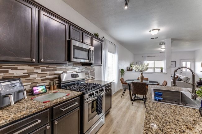 Kitchen with stainless steel appliances, decorative backsplash, light wood-style flooring, dark brown cabinetry, and stone countertops | Image 14