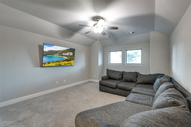 Living area with vaulted ceiling, visible vents, a ceiling fan, baseboards, and carpet flooring | Image 19
