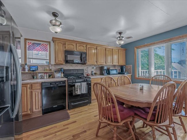 Kitchen with black appliances, tile countertops, healthy amount of natural light, and light wood-type flooring | Image 18