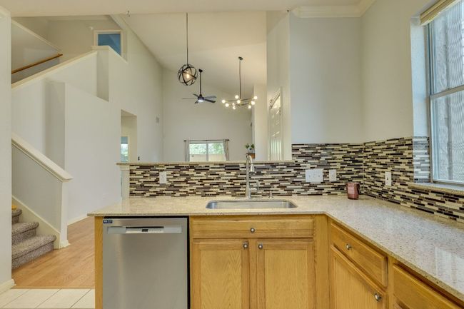 Kitchen with stainless steel dishwasher, backsplash, a peninsula, light stone countertops, and hanging light fixtures | Image 13