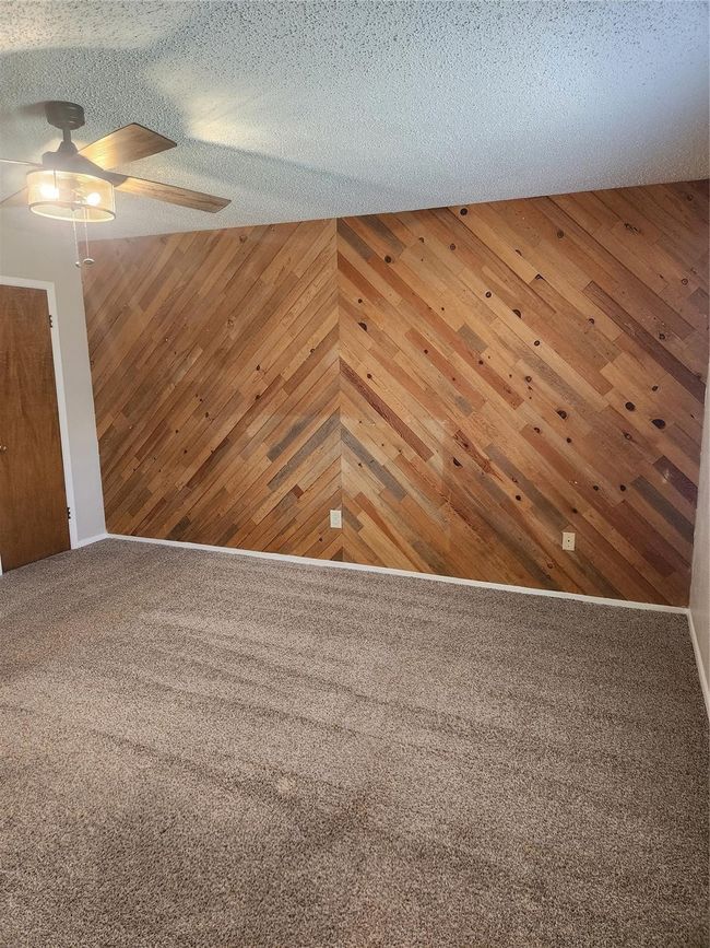 Unfurnished room with ceiling fan, wood walls, carpet, and a textured ceiling | Image 18