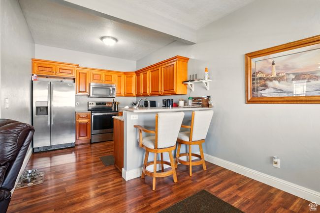 Kitchen with stainless steel appliances, a peninsula, dark wood-type flooring, light countertops, and baseboards | Image 11