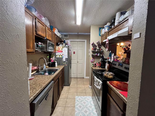 Kitchen with appliances with stainless steel finishes, a textured wall, light tile patterned flooring, a textured ceiling, and under cabinet range hood | Image 4
