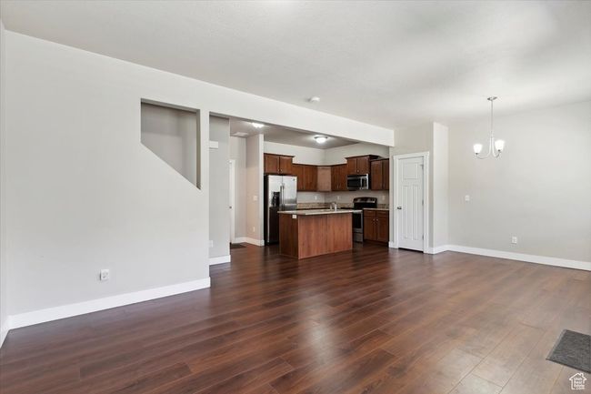 Unfurnished living room with a chandelier, dark wood-style floors, and baseboards | Image 9
