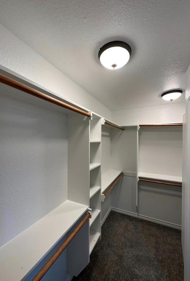 Walk in closet featuring dark colored carpet | Image 11