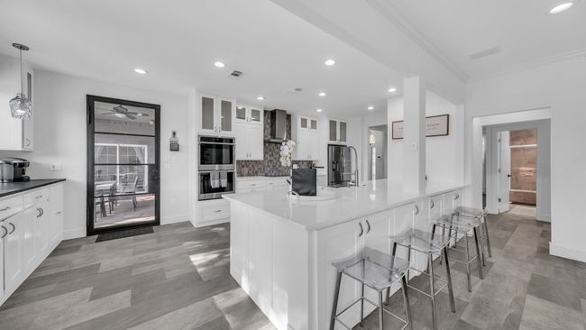 Kitchen featuring appliances with stainless steel finishes, wall chimney exhaust hood, a ceiling fan, a breakfast bar area, and backsplash | Image 15