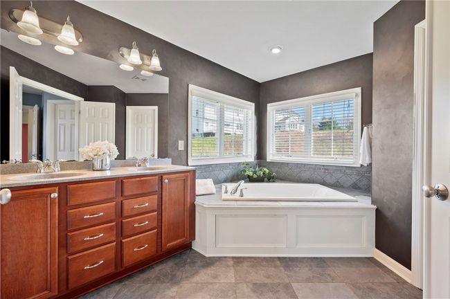 The primary bath offers a double sink vanity, garden tub with tile surround, tiled floors and a walk-in shower. | Image 17