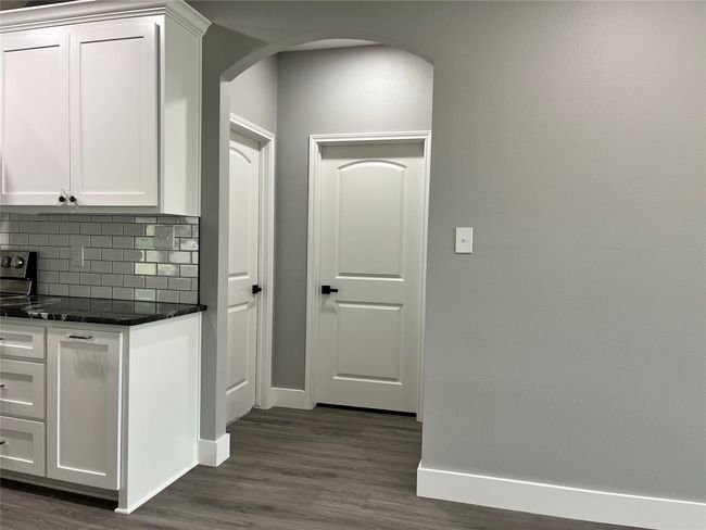Kitchen with tasteful backsplash, dark wood-type flooring, white cabinetry, arched walkways, and dark stone countertops | Image 20