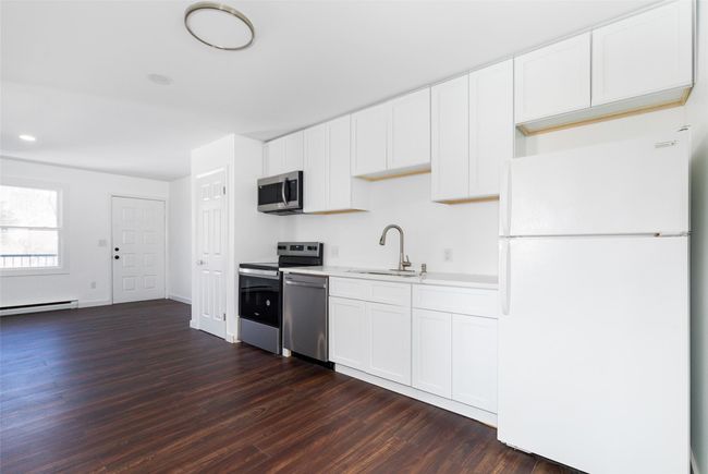 Kitchen with light quartz countertops, appliances with stainless steel finishes, dark wood-type flooring, white cabinetry, and a sink | Image 7