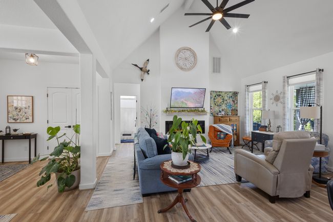 Living room with high vaulted ceiling, a ceiling fan, visible vents, wood finished floors, and baseboards | Image 7