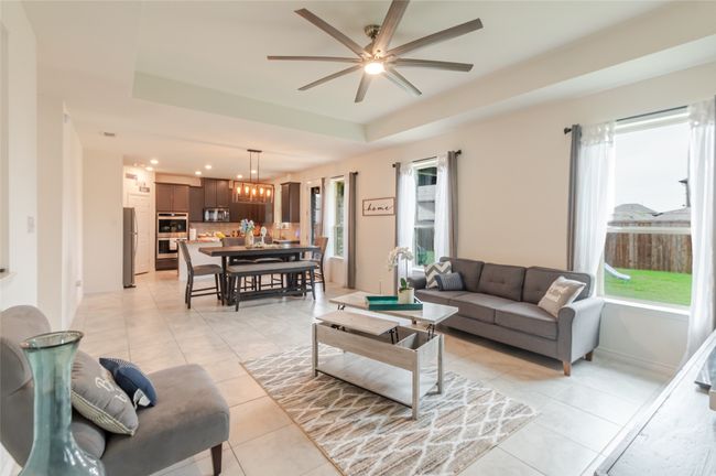 Living area with a raised ceiling, ceiling fan with notable chandelier, light tile patterned floors, and a healthy amount of sunlight | Image 4