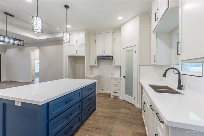 Kitchen with white cabinetry, hanging light fixtures, sink, and a kitchen island | Image 17