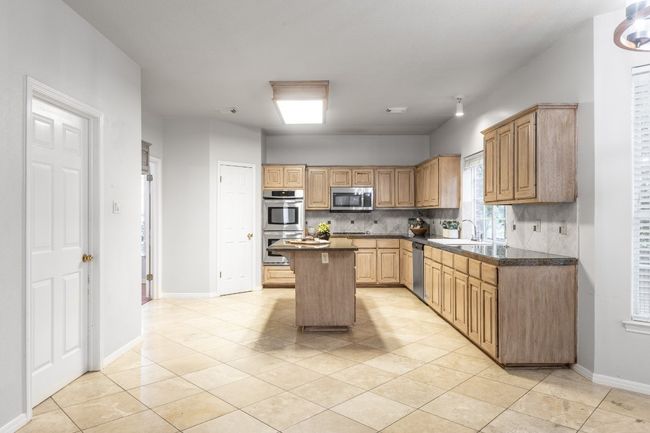 Kitchen with appliances with stainless steel finishes, a kitchen island, decorative backsplash, and light tile patterned floors | Image 13