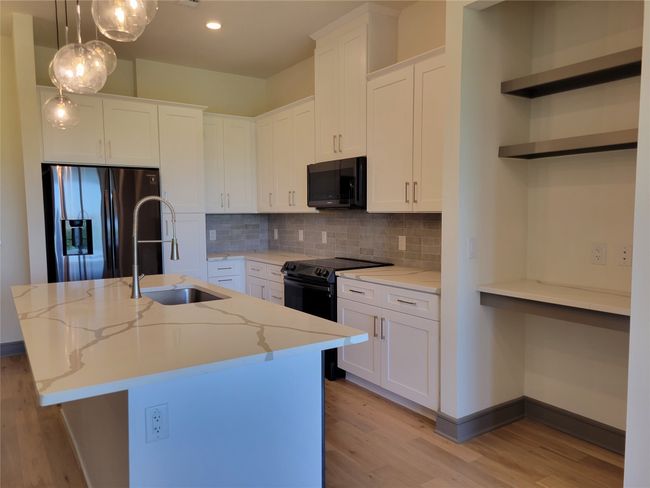 Kitchen with fridge with ice dispenser, black electric range, a sink, light wood finished floors, and a center island with sink | Image 7